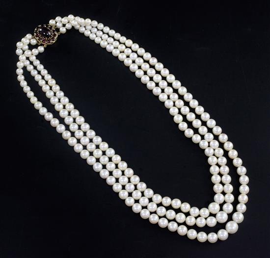 A triple strand graduated cultured pearl necklace with garnet cluster set oval gold clasp, 60cm.